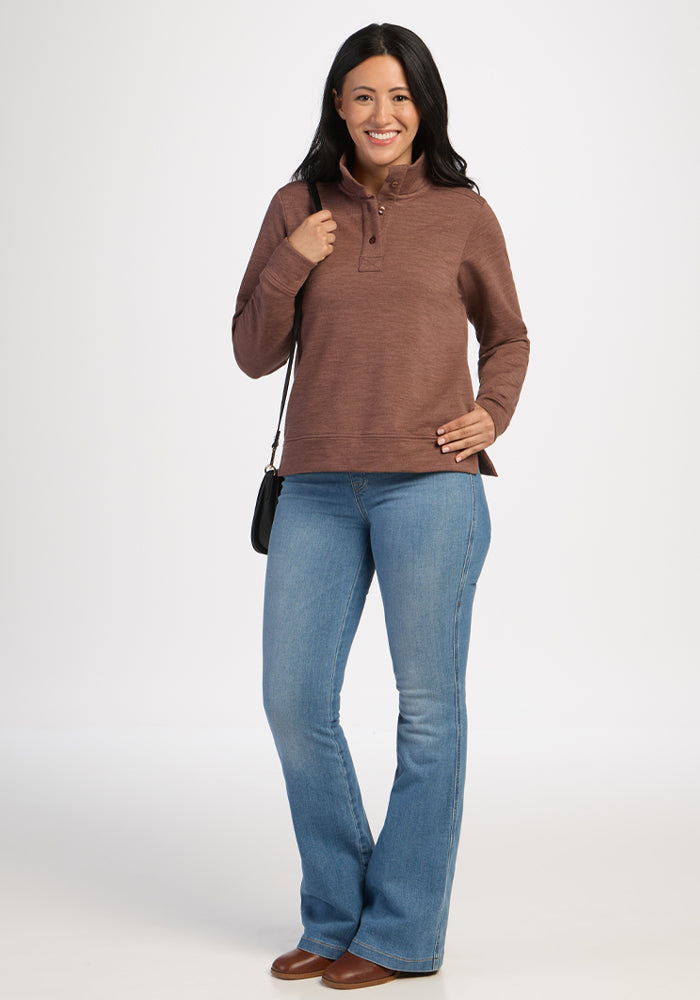 Woman wears Woolx Annie 3 Button Pullover in Sable Heather, blue jeans, brown shoes, smiling with black shoulder bag.