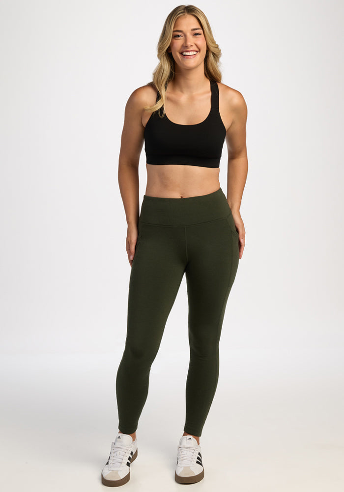 Smiling woman in Woolx Frost Leggings - Duffel Bag, black sports bra, and white sneakers stands on a white background.