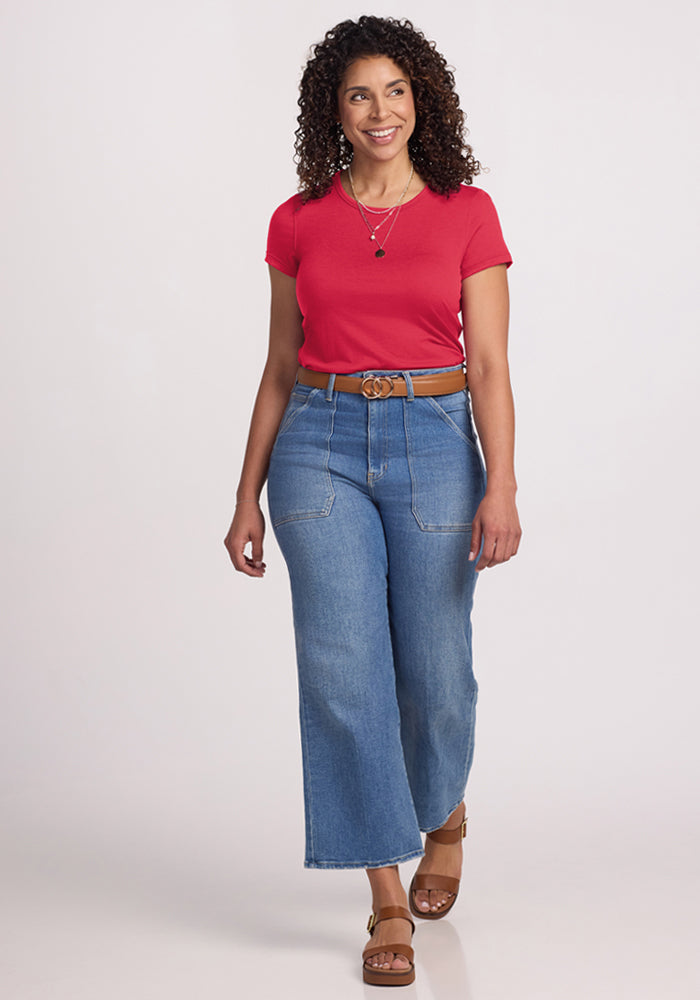 Woman in a Woolx Addie Crew Neck - Berry Ice Pop Merino tee, wide-leg jeans, sandals, and a belt, smiling.