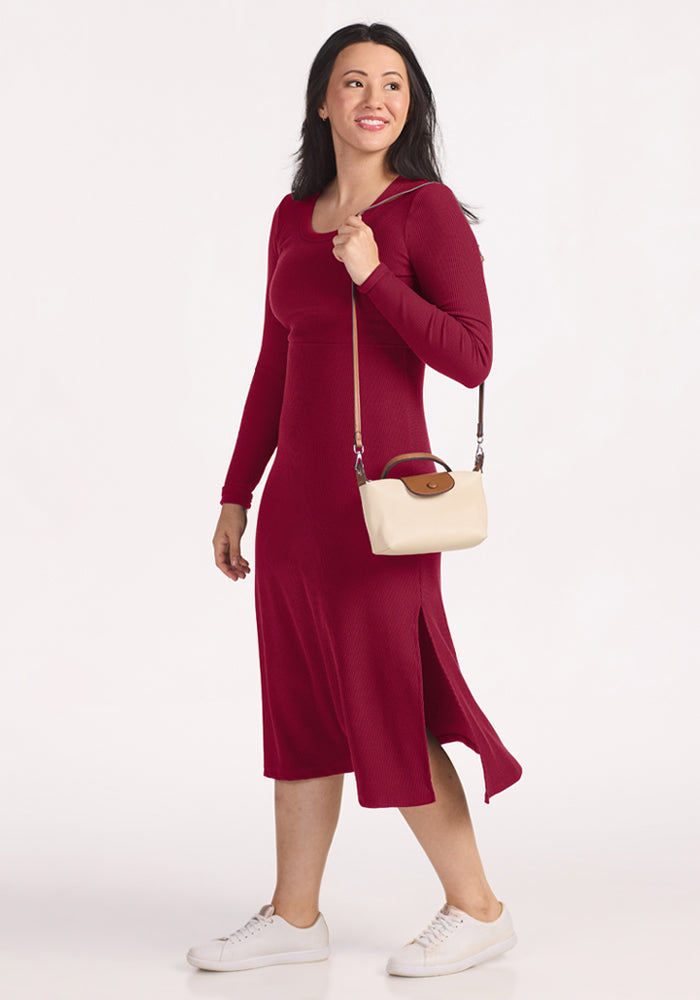 Woman in a Woolx Caroline Ribbed Twirl Dress - Beet Red, white sneakers, cream handbag, walking and smiling.