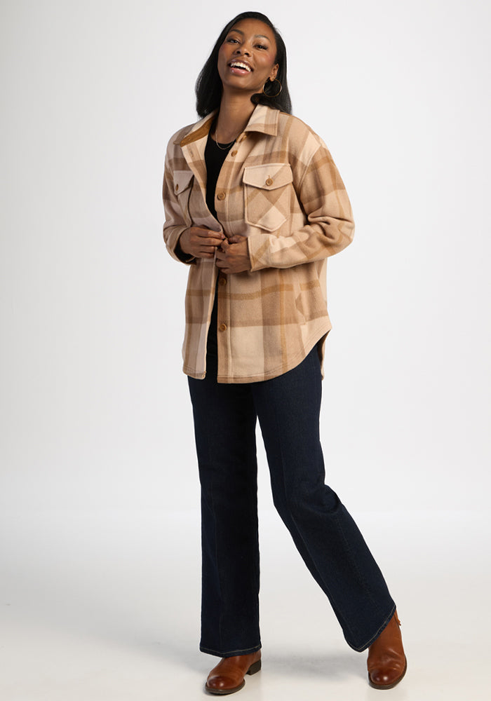 Woman wears Woolx Sawyer Shacket in Saddleback Plaid, black shirt, dark jeans & brown boots, smiling on white.