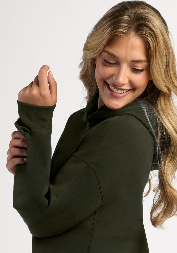 A smiling woman wearing a dark green merino wool Genevieve Hoodie - Duffel Bag.