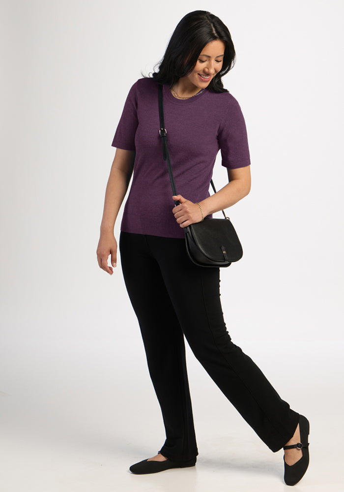 Woman with black hair in Woolx Anna Crew Sweater - Purple Iris, black pants, flats, crossbody bag on white background.