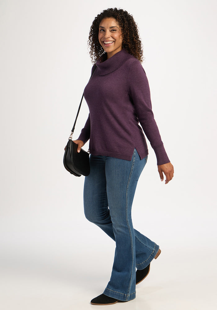 Woman in the Woolx Josie Cowl Neck Sweater - Purple Iris smiles, walking with jeans, black boots, and a shoulder bag.