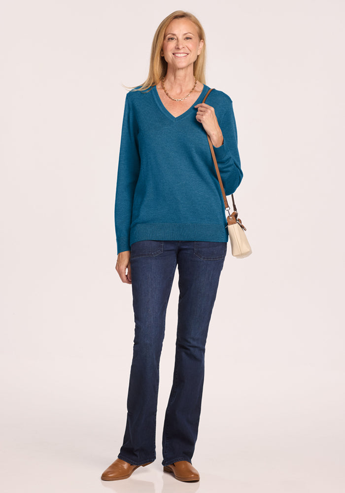Woman in Woolx Francesca Sweater - Blue Pine, jeans, tan shoes, with beige purse against a plain background.