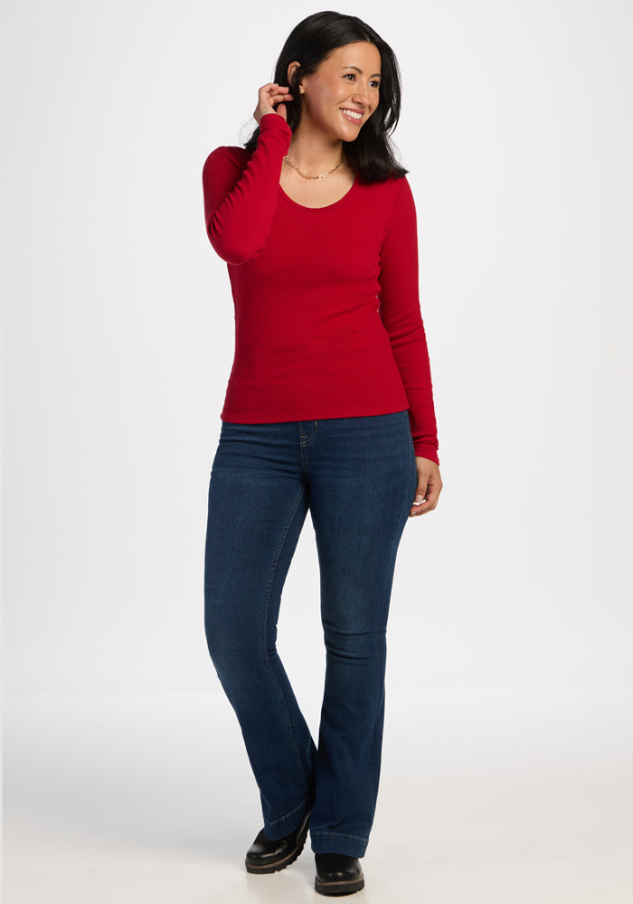 Woman in Woolx Katie Ribbed Long Sleeve - Maraschino Cherry and blue jeans smiles against a plain white background.