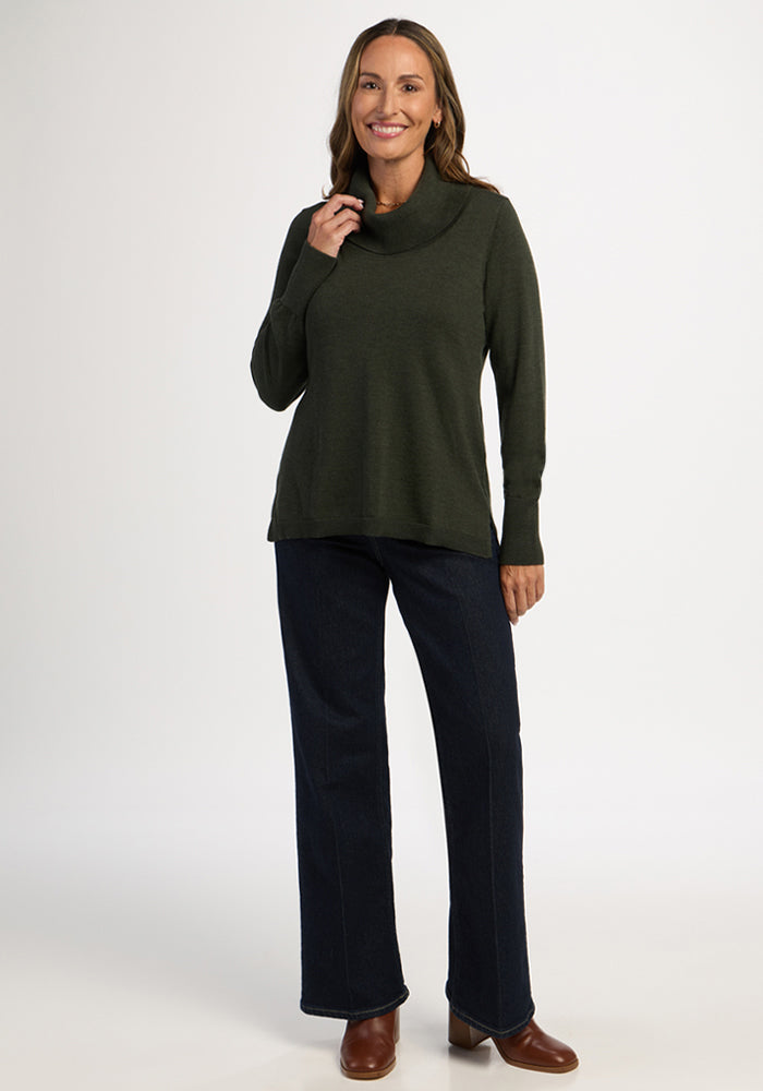 Woman smiles in a Woolx Josie Cowl Neck Sweater in Duffel Bag, dark jeans, and brown boots on a white background.