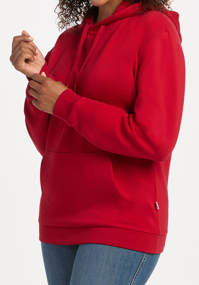 Model wearing Woolx Avery Hoodie - Maraschino Cherry and blue jeans, hands near chest, on a white background.
