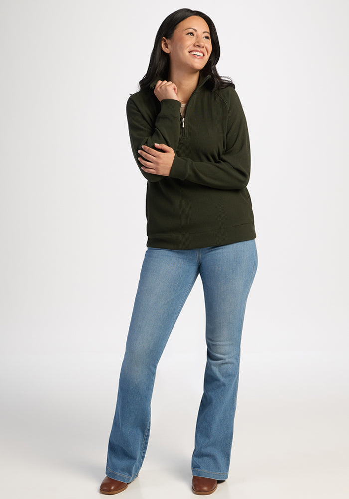 Smiling woman in Woolx Quinn Ribbed 1/4 Zip - Duffel Bag sweater and blue jeans, hand near her face.