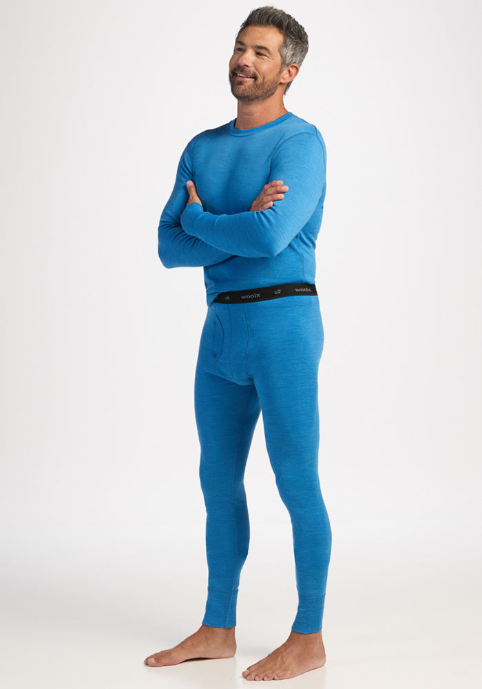 Man in Woolx Backcountry Leggings - Blue Razz stands barefoot, arms crossed, smiling, ready for cold weather comfort.