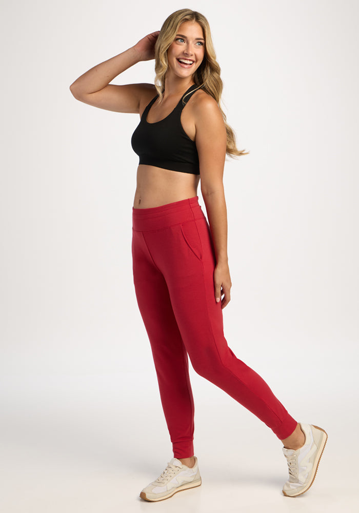 Smiling woman in a black crop top and Woolx Madden Petite Joggers - Maraschino Cherry poses against a white background.
