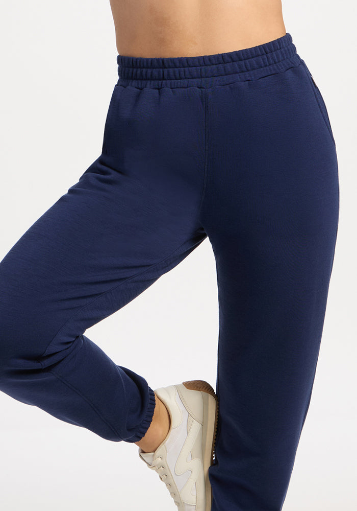 Person in Woolx Parker Sweatpants - Ocean Cavern, white sneakers, one leg bent, on white background.