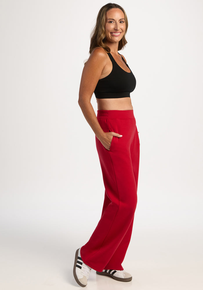 Woman in black crop top and Woolx Bree Lounge Pants - Maraschino Cherry stands sideways, smiling, hands in pockets.