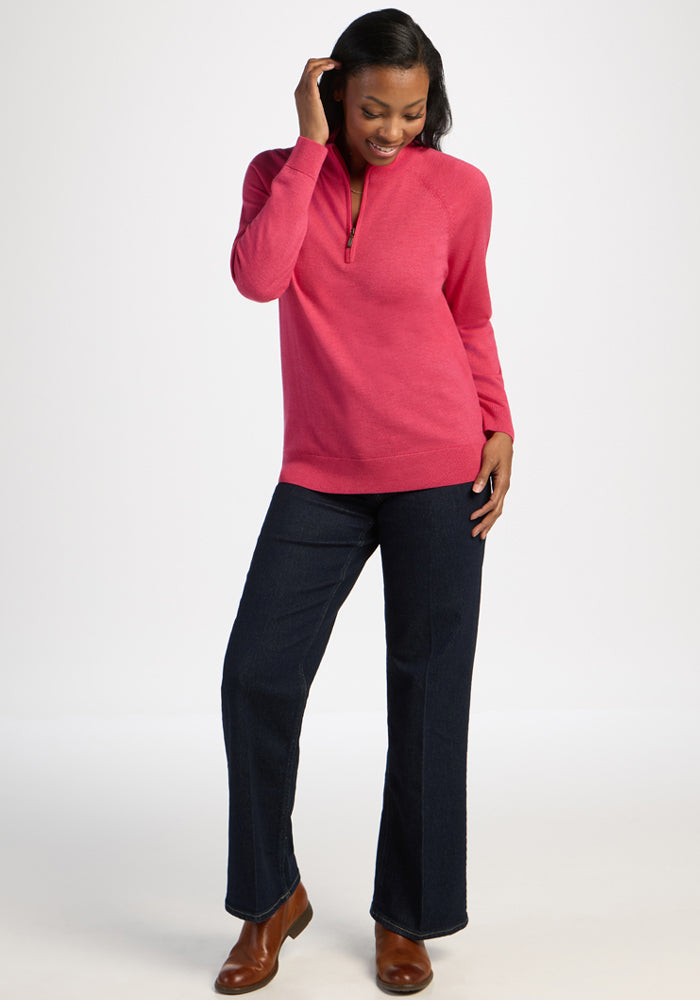 Woman in Woolx Collins Half Zip Sweater in Vivid Rose, dark jeans, and brown boots stands smiling against a white background.