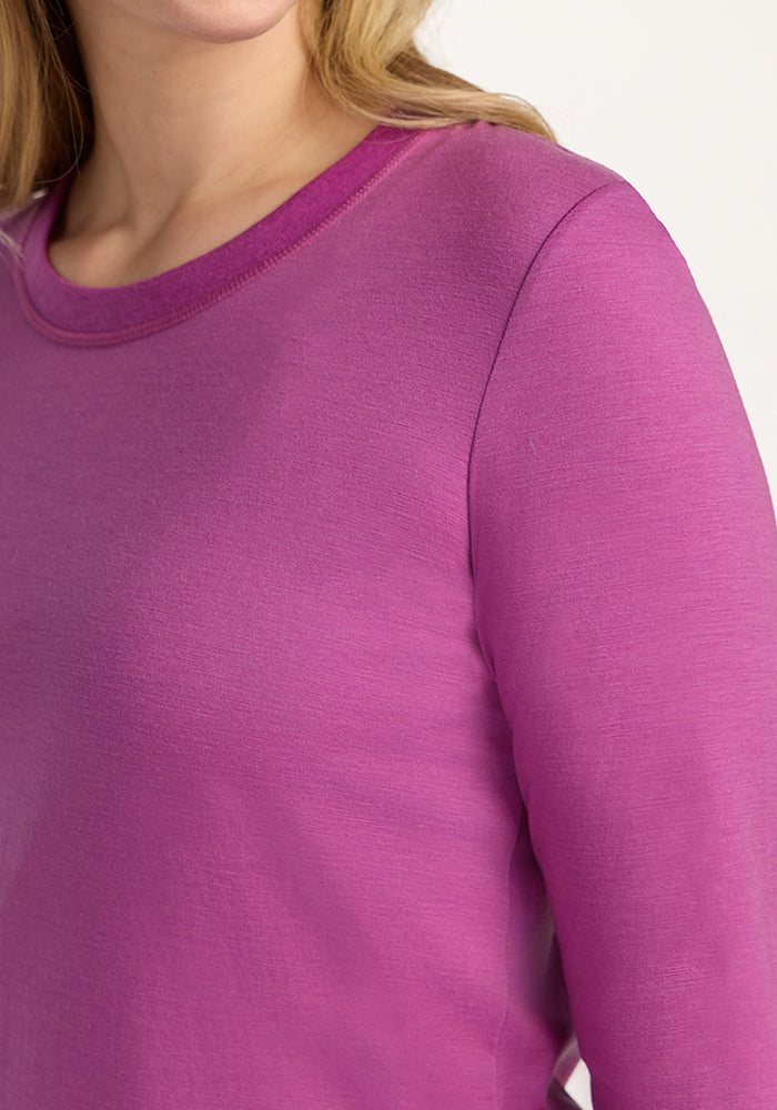 A close-up shows a person wearing the Woolx Hazel Tunic in Purple Wine, with only their lower face, neck, and upper torso visible, highlighting the temperature-regulating Merino wool fabric.