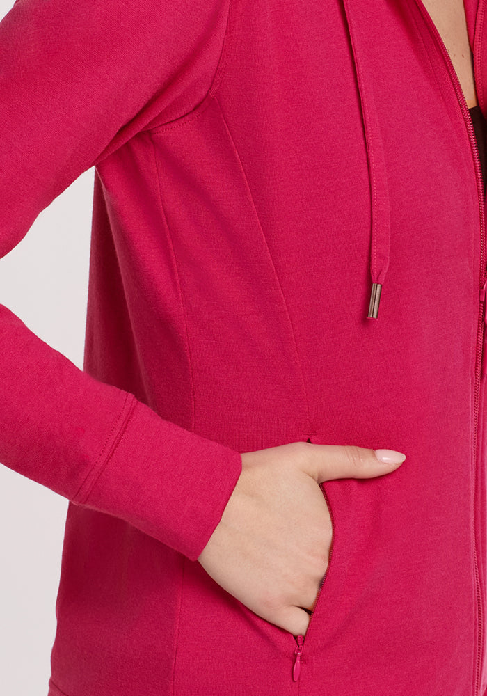 Someone wearing the Woolx Ryann Hoodie in Poppy Spark, with their right hand partly in the pocket, stands against a plain light background.