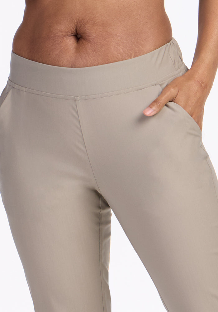 A close-up of someone wearing Woolx Nicole Ankle Pants in Vintage Khaki, with their right hand in the pocket and waistband visible. The plain white background highlights the lightweight design.