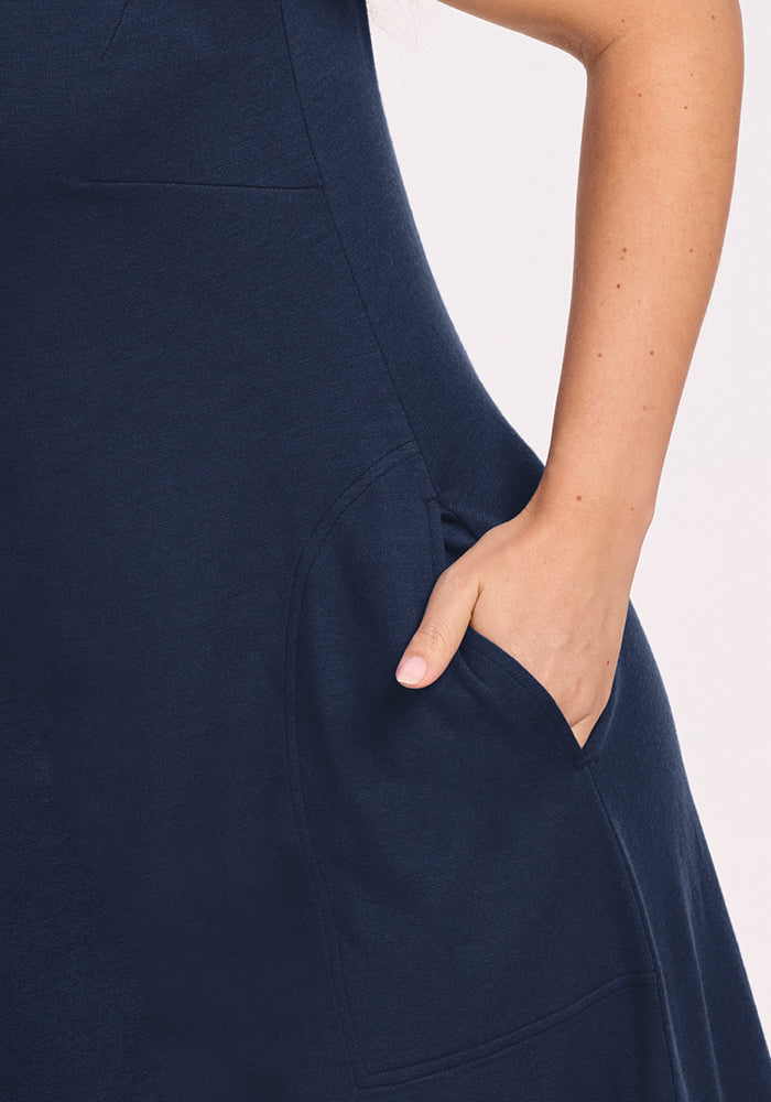 Close-up of a person wearing the Woolx Cassie Dress in Deep Navy, showing their right hand in a side pocket. The light, neutral background highlights the fabric and flattering fit of this wrinkle-resistant travel dress.