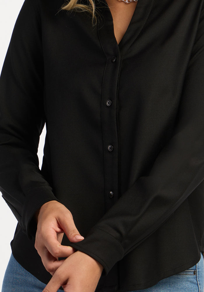 Person in a black Woolx Lorelai Button Up and blue jeans adjusts their sleeve against a plain background.