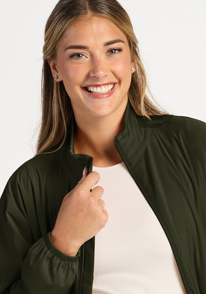 Smiling woman wearing a Cooper Windbreaker - Duffel Bag in olive green over a white shirt.