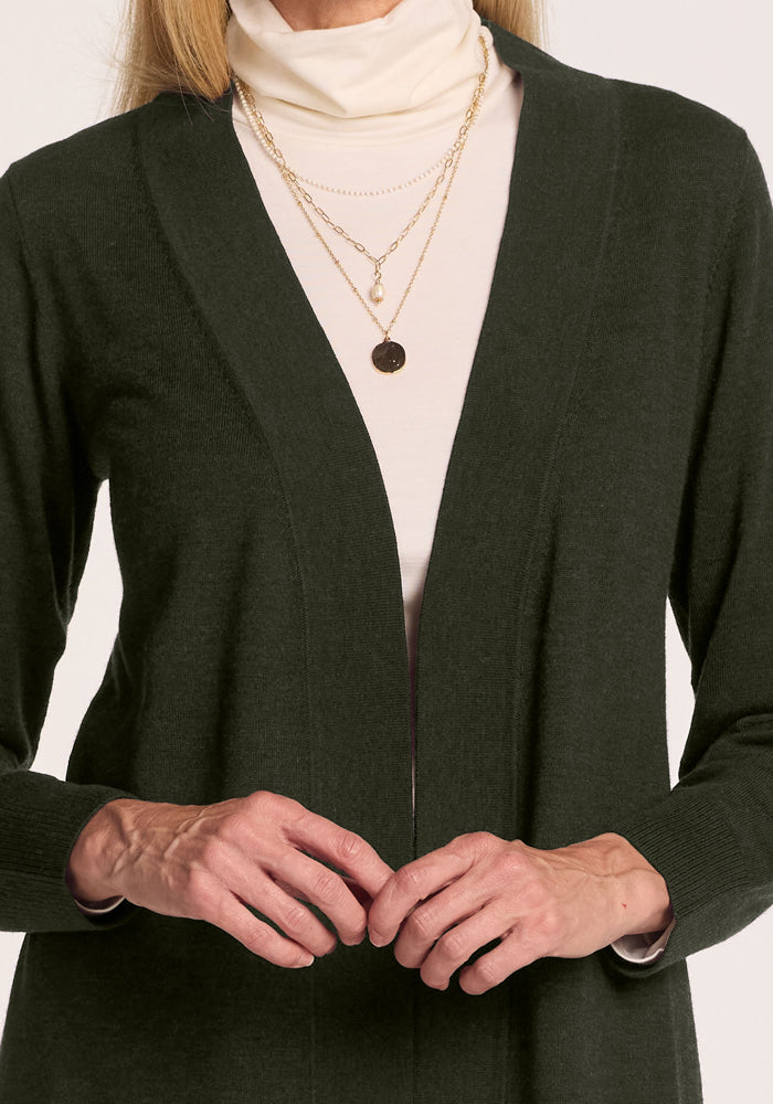 Woman in Woolx Macie Sweater - Duffel Bag and cream turtleneck, layered gold necklaces, hands gently clasped.