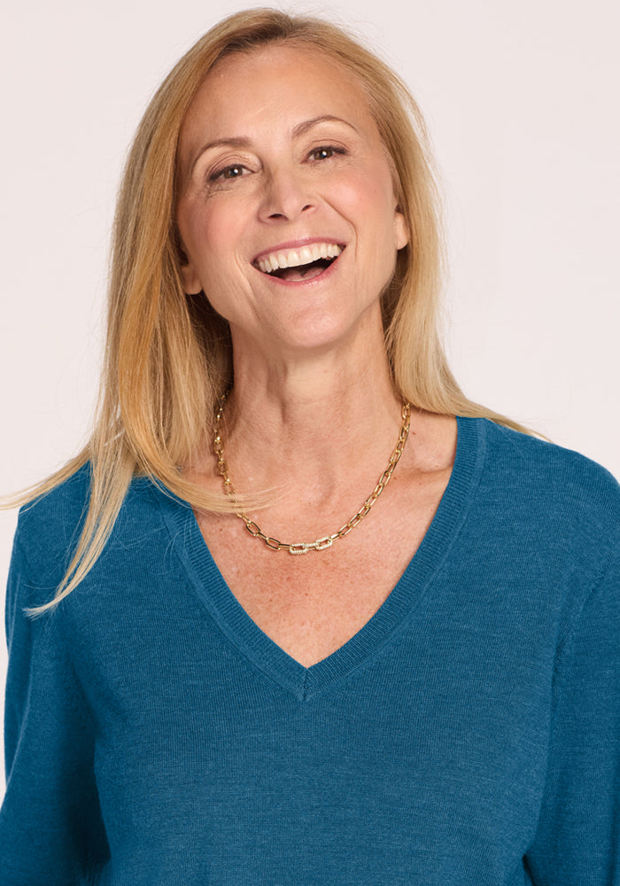 Smiling woman with long blonde hair in a Woolx Francesca Sweater - Blue Pine and a gold chain necklace.