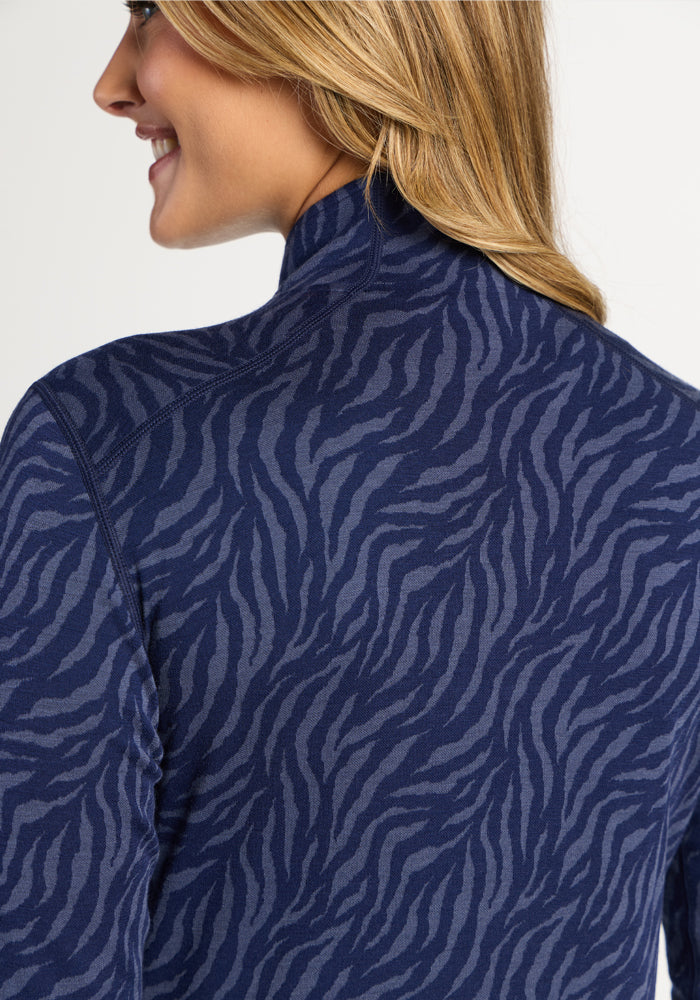 Blonde woman smiles in Woolx Emi 1/4 Zip – Midnight Safari, with a Merino wool layer and zebra-print jacket.