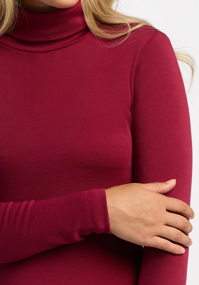 Woman in Woolx Peyton Turtleneck - Beet Red, right hand on left arm, wearing long-sleeve Merino wool style.