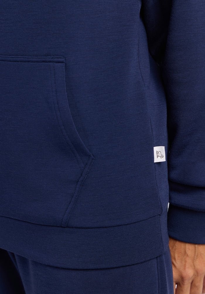 Close-up of a person in the Woolx Avery Hoodie - Ocean Cavern, a navy sweatshirt with pocket and white seam tag.