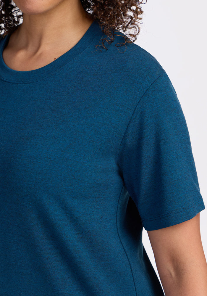 A close-up of a person wearing the Woolx Audrey Tee in Majolica Blue. The relaxed-fit, lightweight shirt is shown from the lower face to upper torso with curly hair visible, set against a plain white background.
