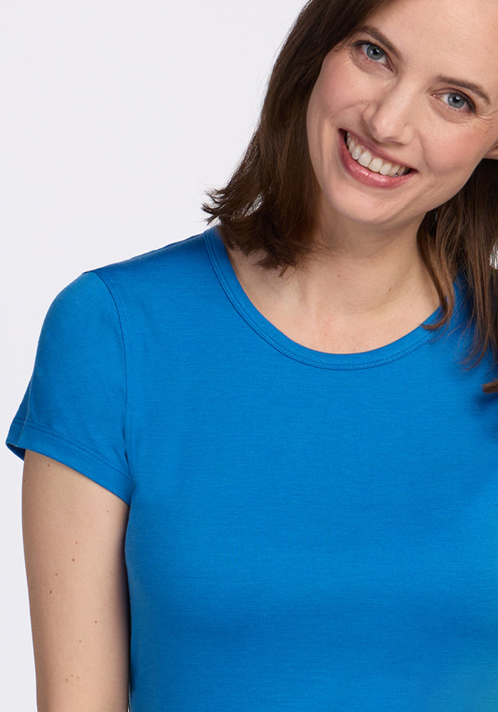 A woman with shoulder-length brown hair, wearing the Woolx Addie Crew Neck - Wave Rider top, smiles and slightly tilts her head against a white background.