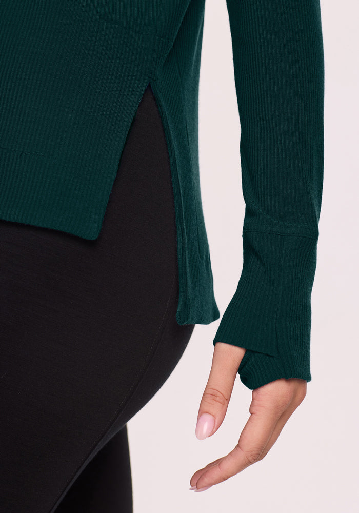 Close-up of a person wearing the Woolx Ainsley Sweater in Deep Pine with thumb holes and black leggings.