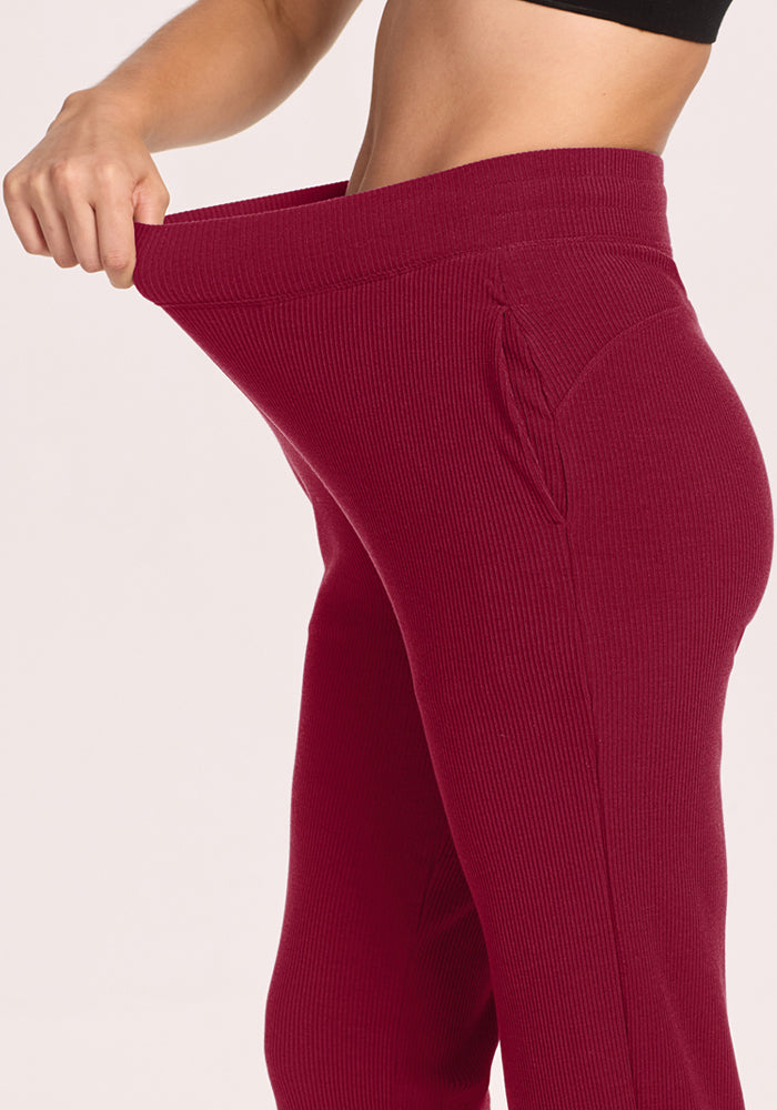 Woman in black top stretches waistband of Woolx Luca Petite Pants in Beet Red, showing comfy ribbed Merino wool.