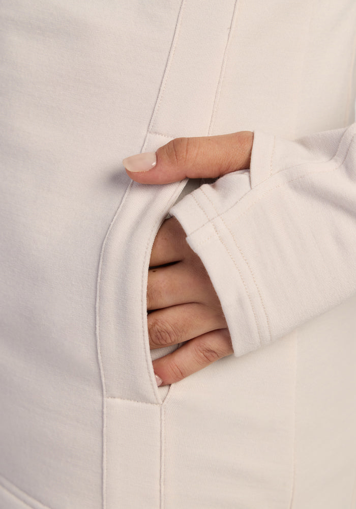 Thumb peeks from a cozy Zoey Zip Up Hoodie by Woolx in Ecru—a perfect cold-weather pick.