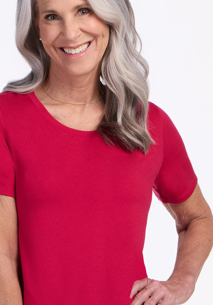 Smiling older woman with long gray hair wears the Woolx Georgie Dress in Poppy Spark. She stands confidently against a light background. The Merino wool dress is ideal as a temperature-regulating, travel-friendly option.