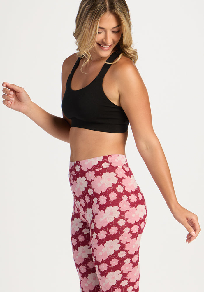 Woman smiling in Woolx Taylor Baselayer Leggings - Floral Crush and a black sports bra against a white background.