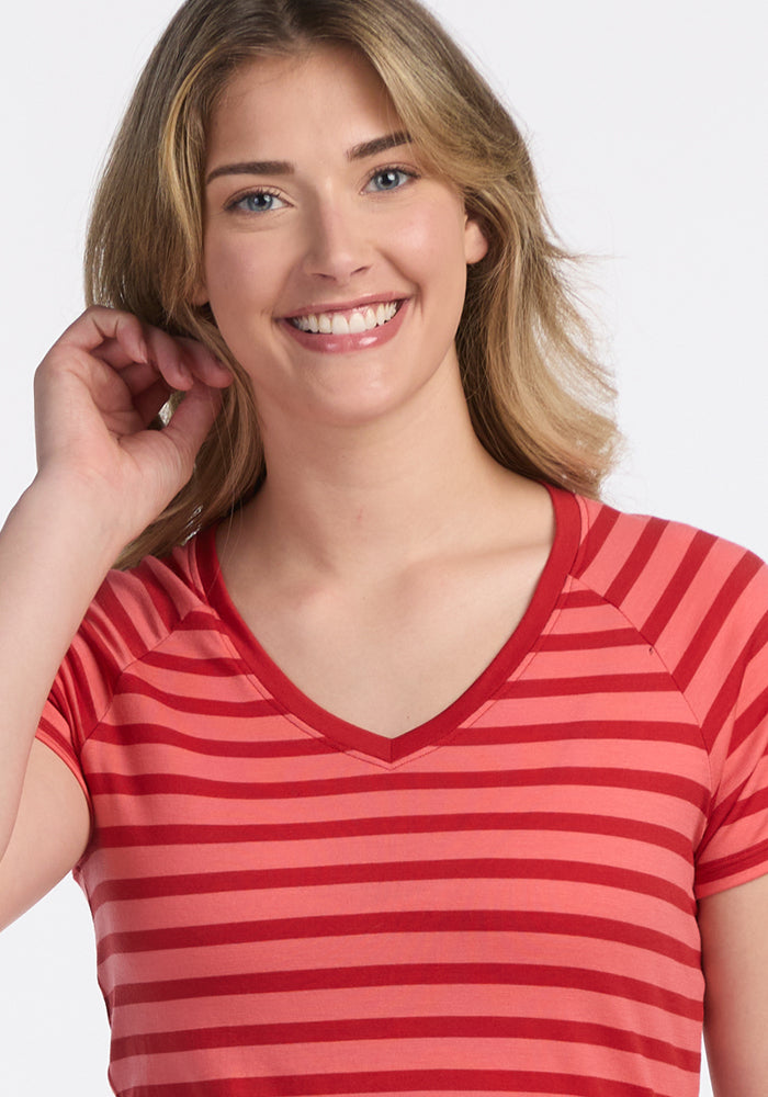 A smiling person with blonde hair models the Woolx Mia V Neck - Wildberry Stripe, a women’s Merino wool tee. Its odor-resistant, moisture-wicking fabric keeps them comfortable all day as they pose against a plain white background.