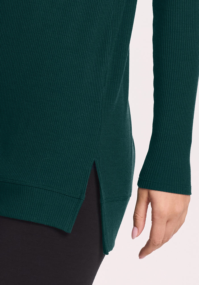 Close-up of someone in the Woolx Evie Ribbed Tunic - Deep Pine with black pants, a cozy, temperature-regulating outfit.