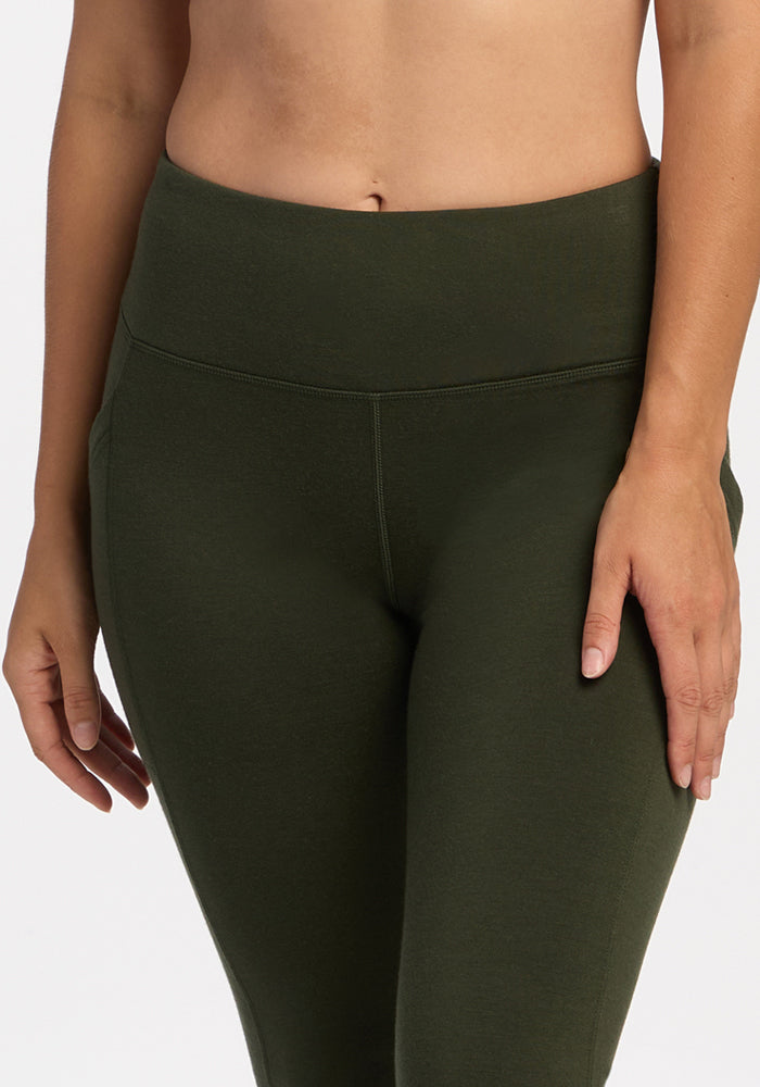 Model in Woolx Frost Leggings - Duffel Bag, high-waisted, dark green, posing with hand on thigh against plain background.