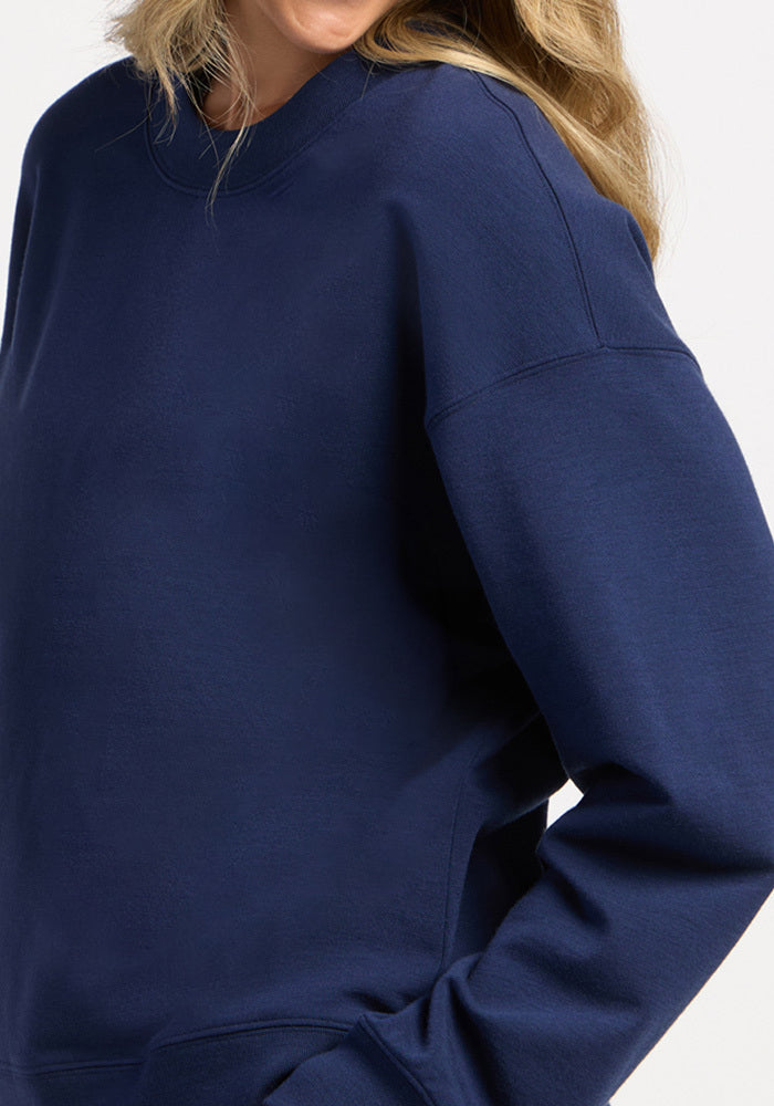 A person wearing a solid dark blue, moisture-wicking merino wool Molly Crewneck - Ocean Cavern sweatshirt.