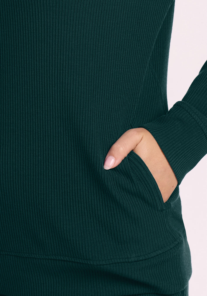 Hand with light pink nails in the pocket of a Woolx Quinn Ribbed 1/4 Zip - Deep Pine sweater.