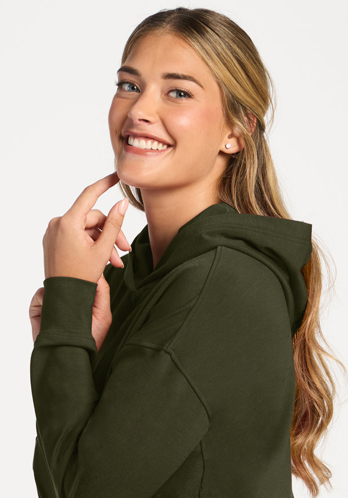 Woman in the Woolx Lizzy Hoodie - Everleaf, touching her face and smiling over her shoulder on a white background.
