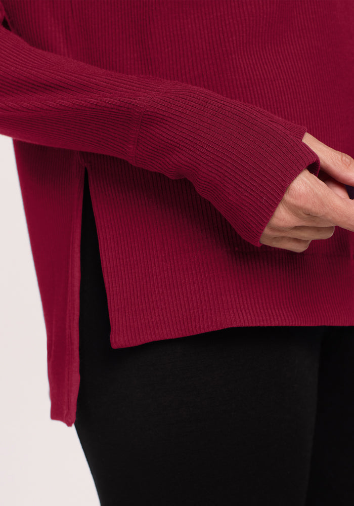 A person in the Woolx Ainsley Petite Sweater in Beet Red with black pants, showing their hand.
