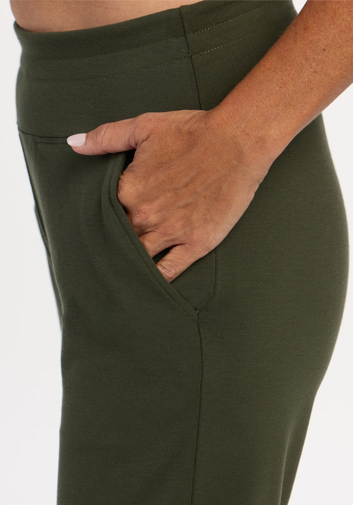 A person wears Woolx Madden Petite Joggers - Everleaf, right hand in pocket, shown from a close-up side view.