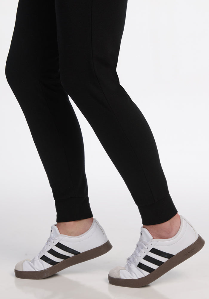 Person wears Woolx Madden Tall Joggers in black and white sneakers with black stripes, standing on a white background.