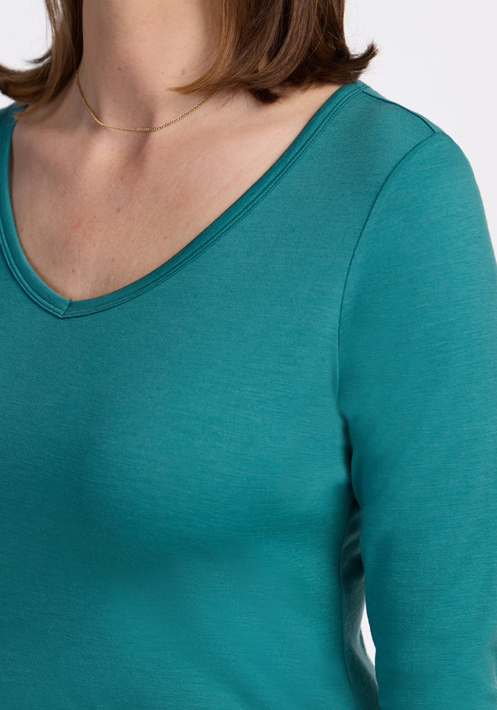 A person wearing the Woolx Layla V Neck Top in Surfside (teal) and a thin gold necklace, shown from the shoulders to upper chest against a white background.