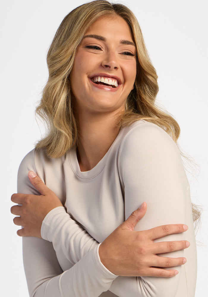 Smiling woman wearing Woolx Sadie Baselayer Top in Ecru, arms crossed, looking sideways in this cozy winter layer.