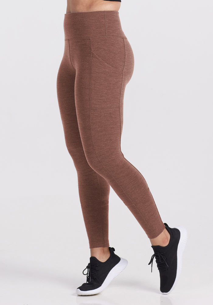 Person wears Woolx Piper Pocket Leggings - Sable Heather and black sneakers, shown from the side on white background.