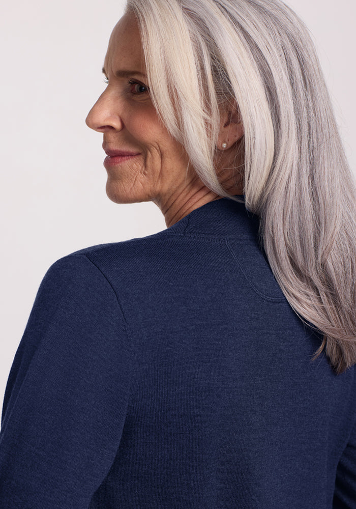 Older woman in the Woolx Macie Sweater - Ocean Cavern, smiling softly and gazing to the side against a plain background.