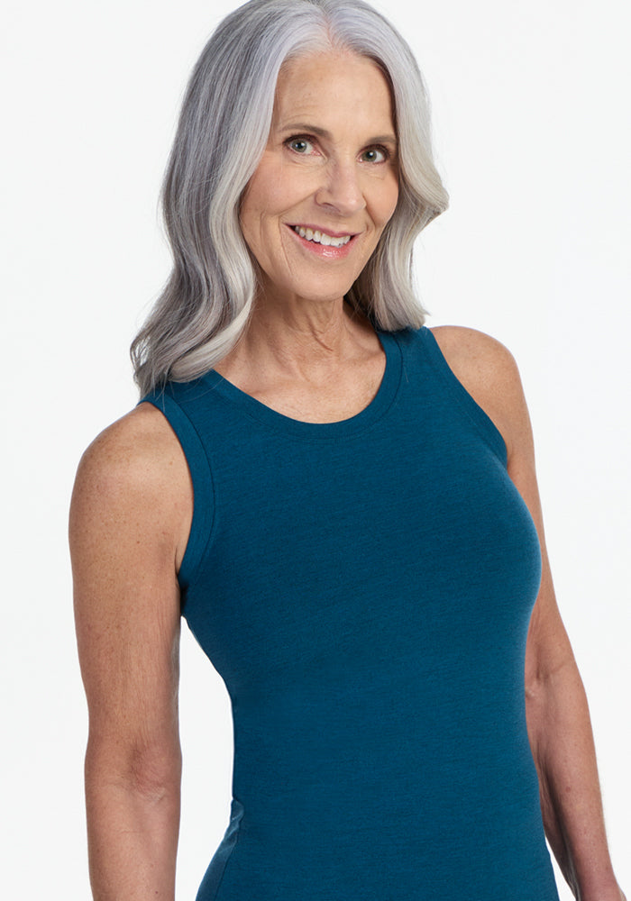 A smiling older woman with long gray hair models the Woolx Ava Tank Top in Majolica Blue, highlighting the comfort and style of this lightweight merino wool women’s base layer against a plain white background.